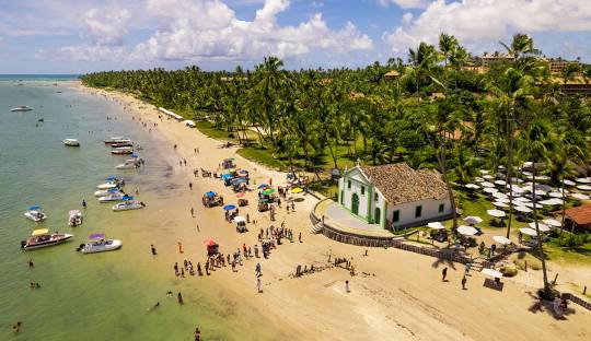 Praia dos Carneiros with iconic white chapel on stilts over crystal clear waters surrounded by palm trees
